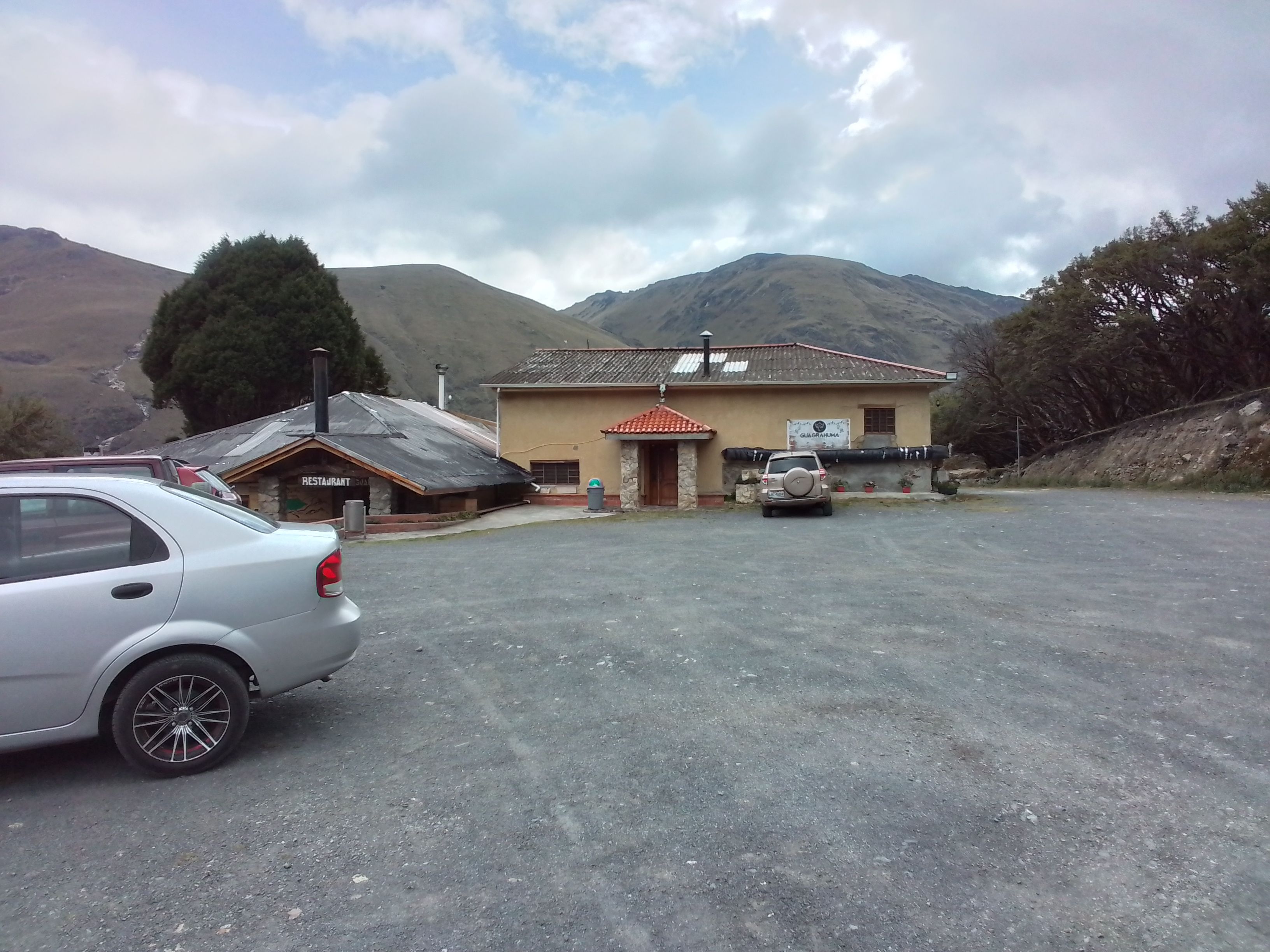 Un bâtiment avec une enseigne indiquant un restaurant, une voiture garée et des montagnes en arrière-plan.