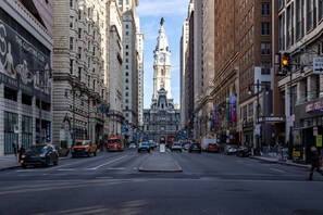 A city street with tall buildings, a prominent clock tower, and various shops and vehicles. - Spruce Villa - 3rd Floor King Studio (Philadelphia)