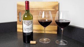 Una bottiglia di vino Camino De Chile, due bicchieri di vino rosso e un tappo su un piano di lavoro.