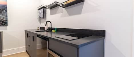 Cuina compacta amb rentaplats integrat, forn d'acer inoxidable, taulell negre i prestatge fixat a la paret sobre l'aigüera.