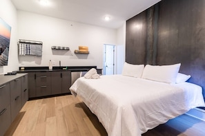 A modern bedroom with a large bed, a built-in wardrobe, a small kitchenette, and a view of the city. - Spruce Villa - 3rd Floor King Studio (Philadelphia)