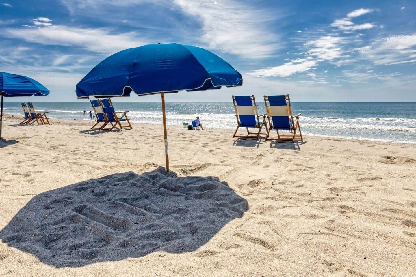 A beach with blue umbrellas and beach chairs.