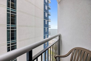 A balcony with a metal railing, a view of a building with multiple windows, and a chair. - 1 Br Couples Beach Escape | Balcony + Resort Pools (Myrtle Beach)