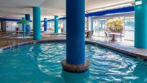 Een binnenzwembad met helderblauw water, omgeven door blauwe pilaren, en een zithoek met tafels en stoelen.