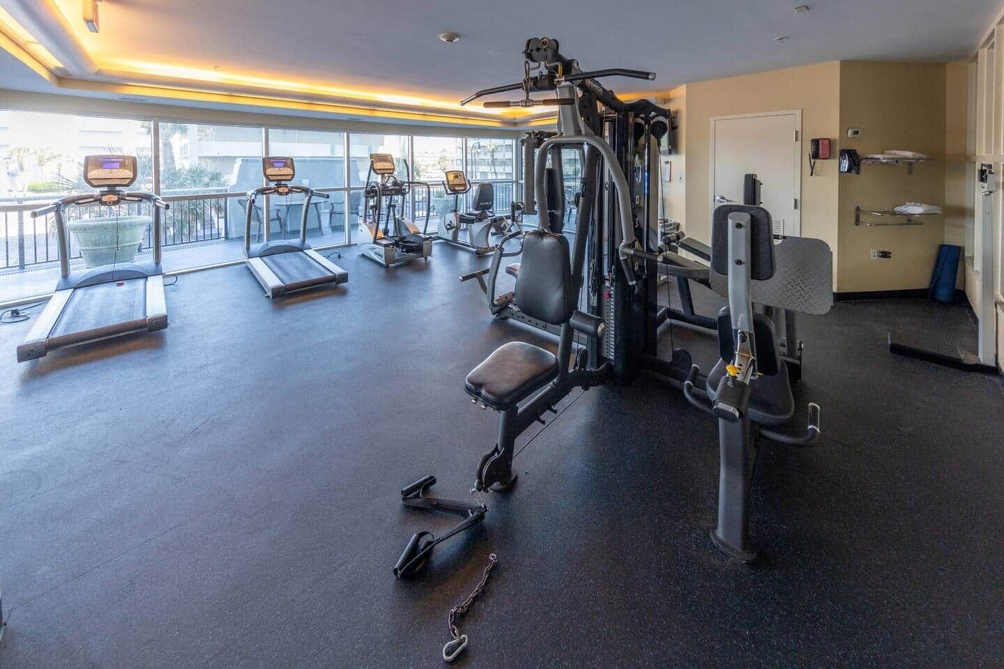 A gym with cardio equipment, weight machines, and a bench.