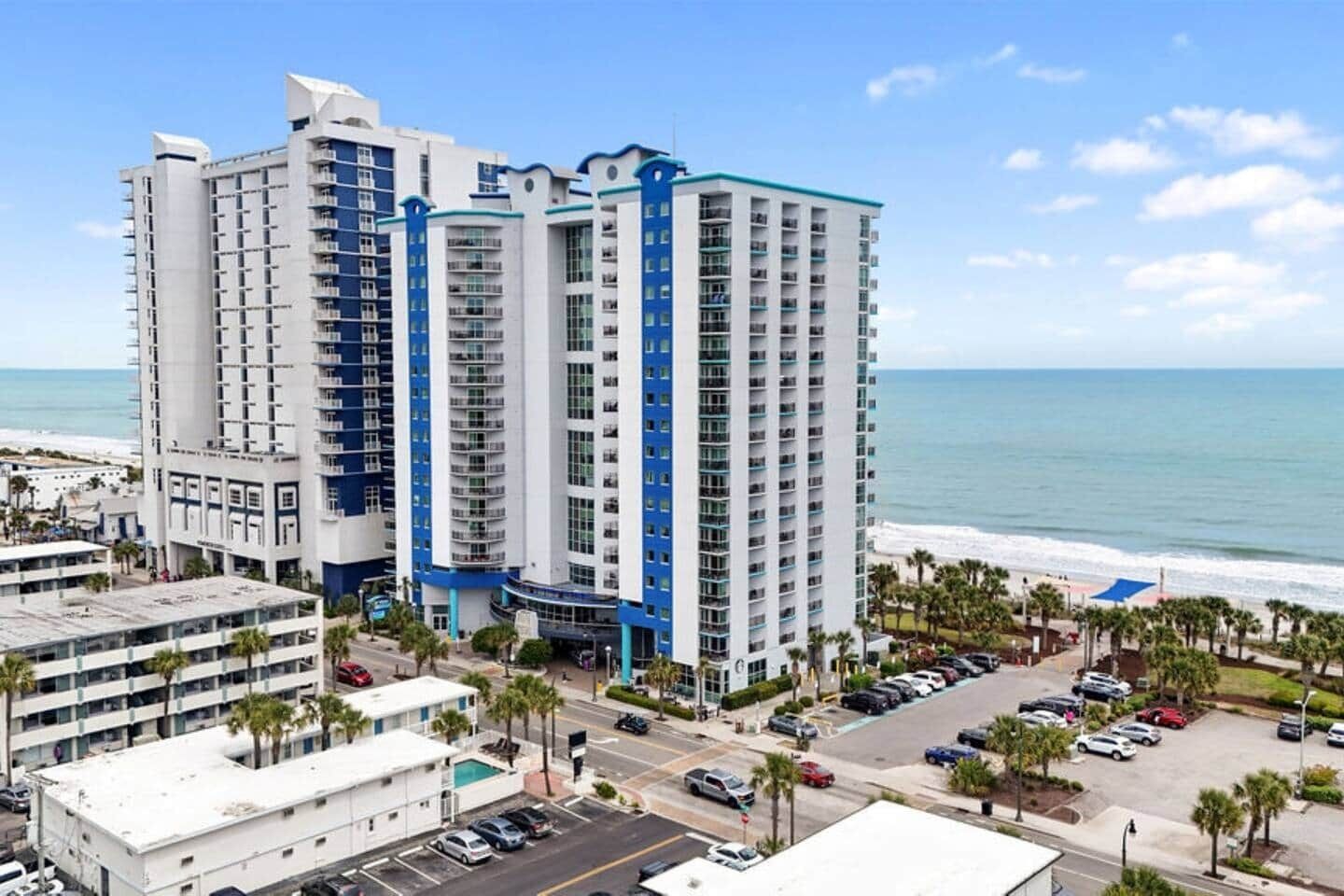 A high-rise hotel with multiple floors, a parking area, and a view of the beach.