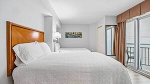 Een hotelkamer met een groot bed, een nachtkastje, een wandlamp, een schilderij en een balkon met gordijnen.