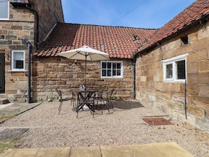 A stone building with a tiled roof, a gravel patio, and a table with chairs under an umbrella. - EWE COTE HALL FARMHOUSE, pet friendly, with open fire in Whitby (Whitby)