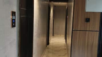 A corridor with a marble floor, wooden paneling on one side, and a door with a digital display.