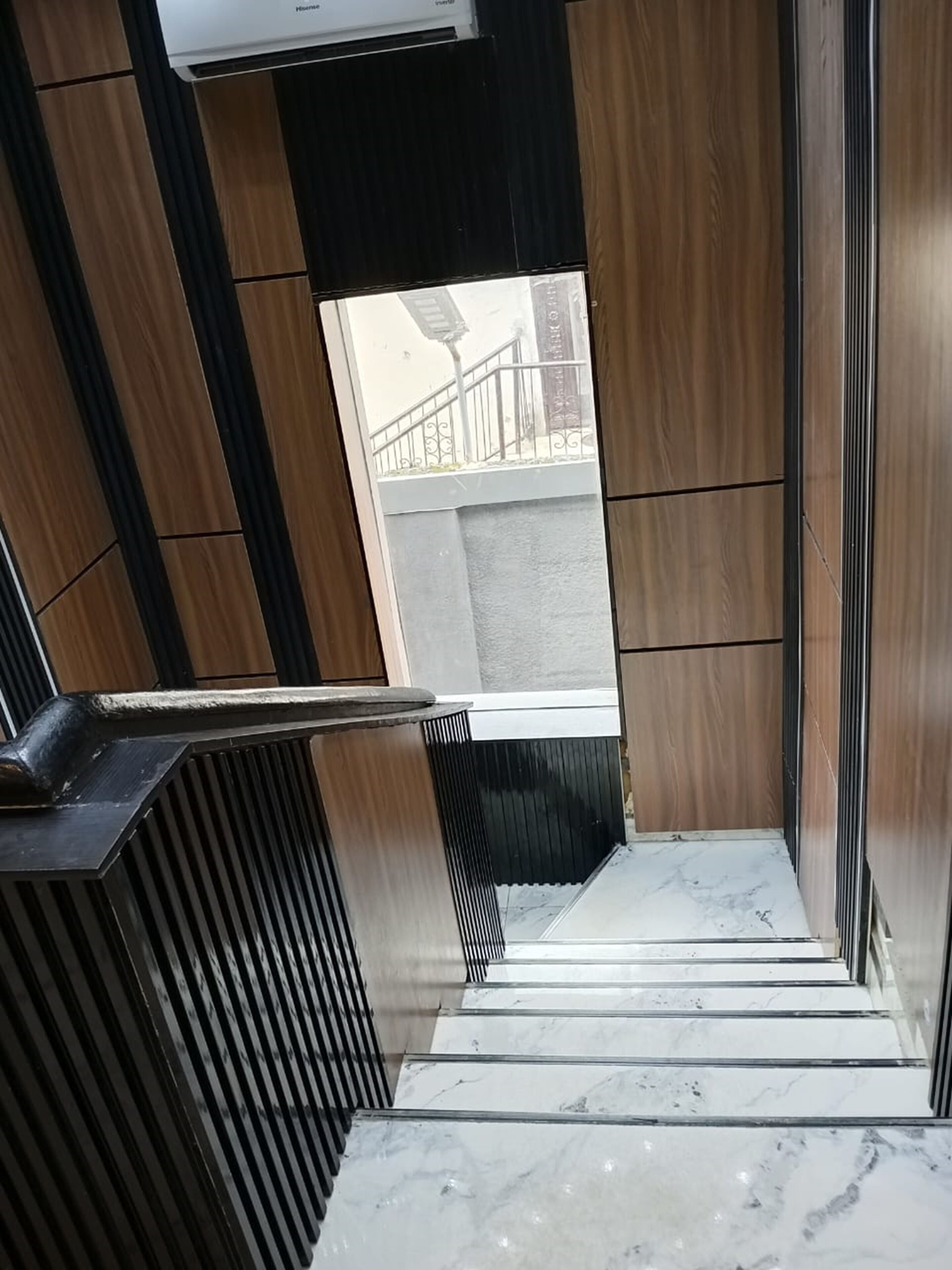 Un interior moderno con una escalera que lleva a un espacio exterior, con paneles de madera y suelo de mármol.