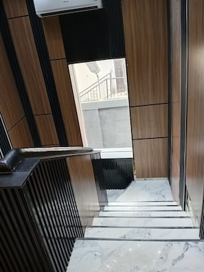 Um interior moderno com escada que leva a uma área externa, combinando painéis de madeira e piso de mármore.