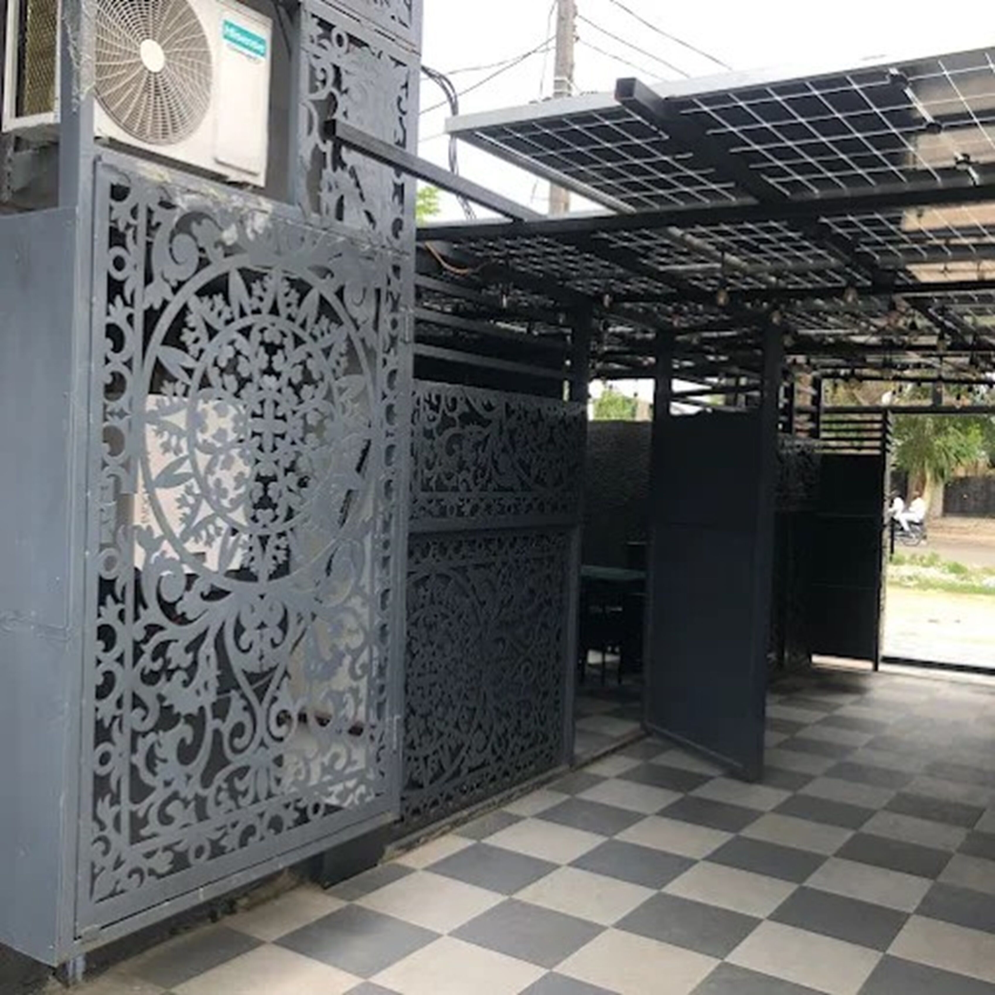 Un espacio exterior techado con una cerca metálica estampada, un ventilador y paneles solares.