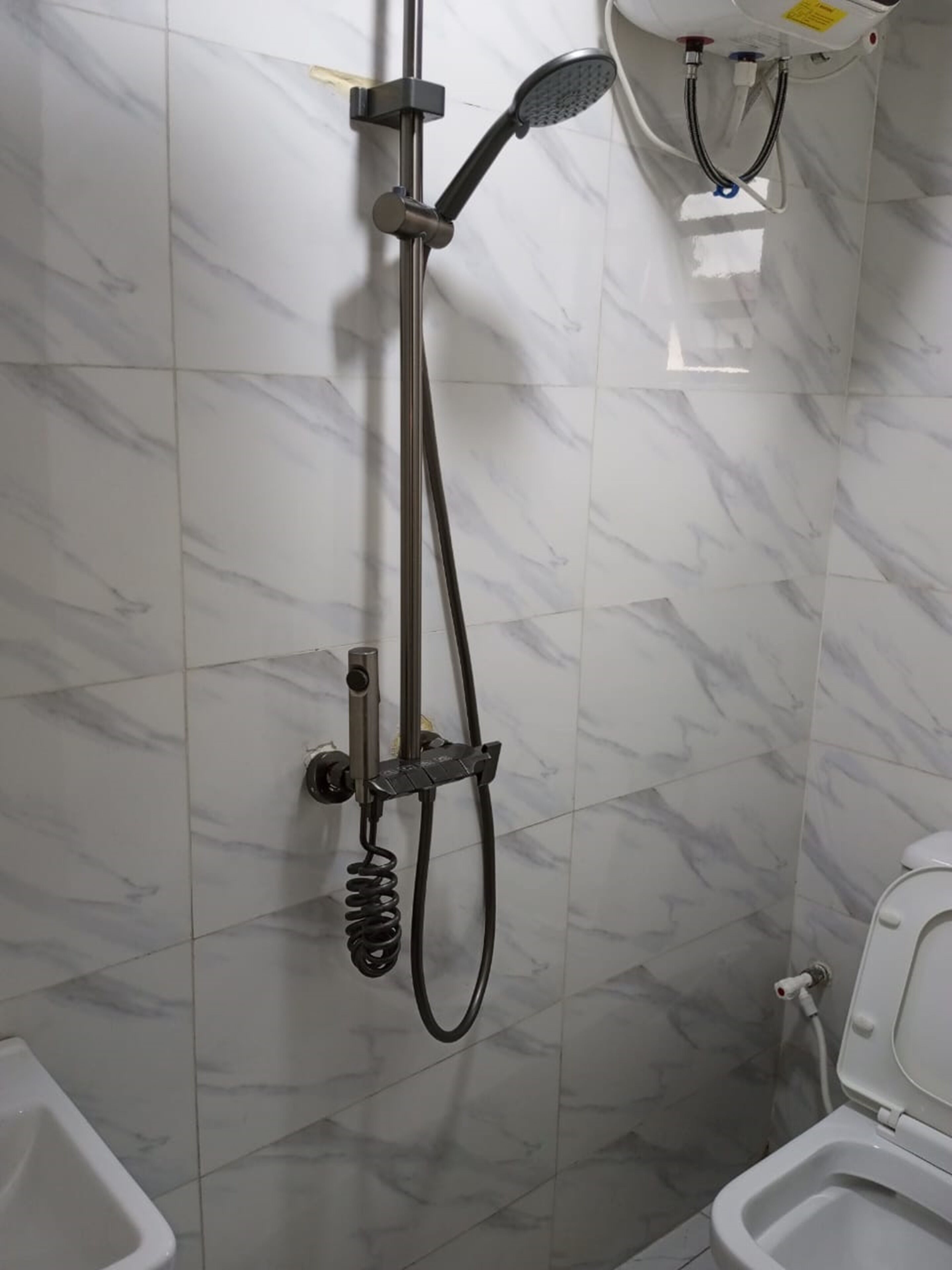 A bathroom with a shower, toilet, and a marble-tiled wall.