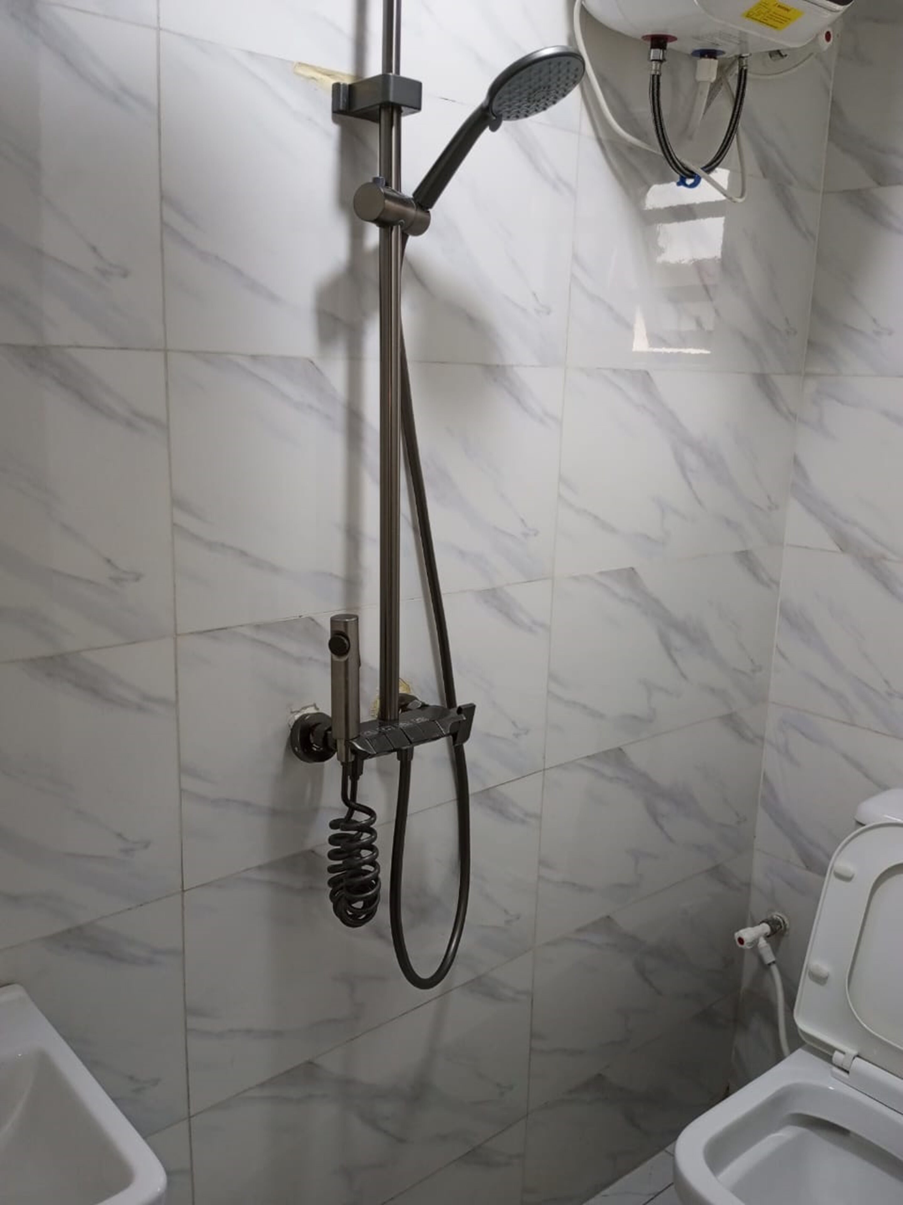 Un baño con ducha, inodoro y pared revestida de mármol.