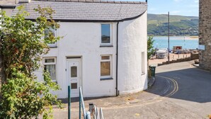 A white building with a door and windows, a stone chimney, and a view of a body of water with boats. - HARBOUR COTTAGE, pet friendly, country holiday cottage in Barmouth (Barmouth)