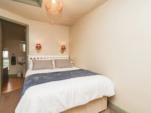 Une chambre à coucher comprenant un lit, deux lampes fixées au mur, un luminaire au plafond, une fenêtre et une porte donnant sur une autre pièce.