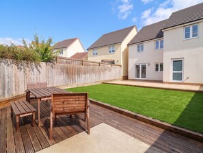 A residential backyard with a wooden deck, a table, and chairs. - HIGHER GORSE, pet friendly, with a garden in Roundswell (Barnstaple)