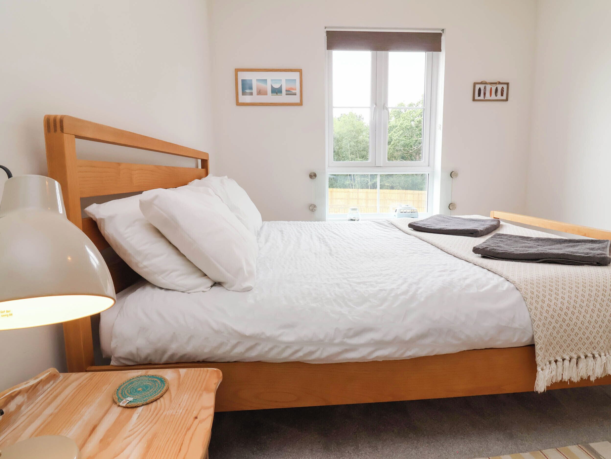 Ein ordentlich bezogenes Bett mit weißer Bettwäsche, einem Holz-Kopfteil und einer Nachttischlampe.