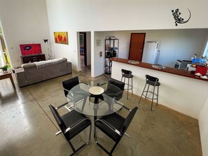 Een moderne leefruimte met een glazen eettafel, zwarte stoelen, een grijze bank en een keuken met een bar.