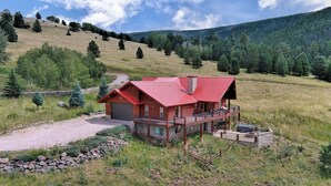 A log cabin with a red roof, a covered porch, and a stone chimney. - Cascade Overlook in Angel Fire (Angel Fire)