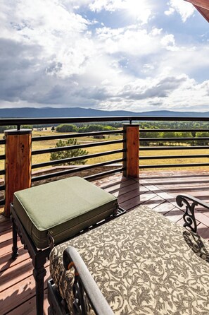 Eine Holzterrasse mit einer Bank und einem grünen Koffer, mit Blick auf eine Landschaft mit Bergen und Feldern.