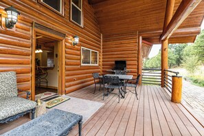 Eine Holzhütte mit einer Terrasse, einem Essbereich mit Metallstühlen und einem Tisch sowie einem Grill außen.