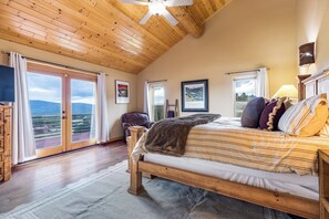 Ein Schlafzimmer mit Holzboden, einem Bett mit gestreifter Bettwäsche, einem großen Fenster mit Aussicht und einem angebrachten Fernseher.