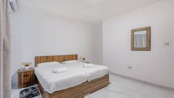 Habitación de hotel con una cama de madera, ropa de cama blanca, una mesita de noche con un florero y un espejo en la pared.