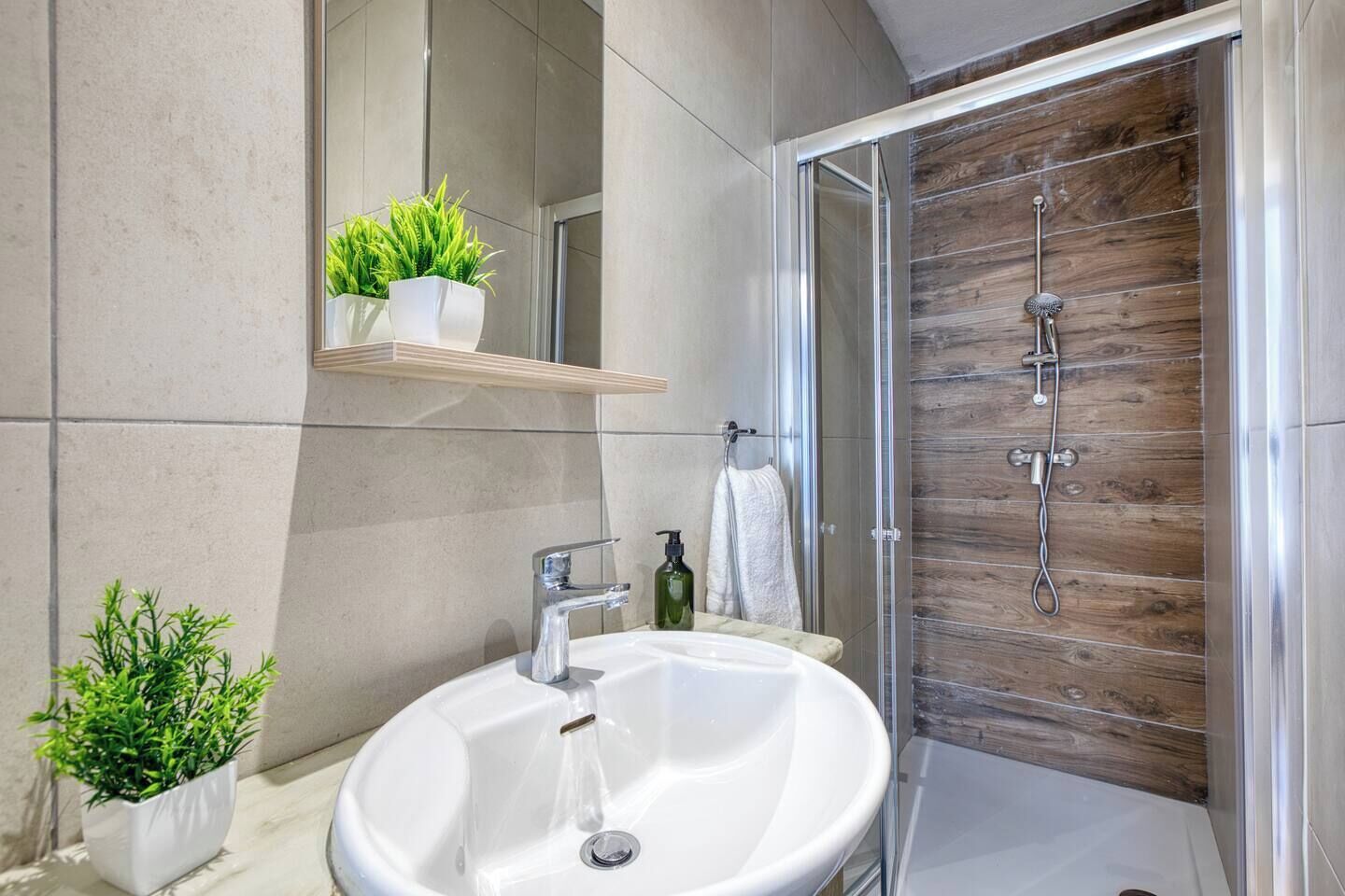 A modern bathroom with a white sink, a glass shower enclosure, and wooden wall paneling.