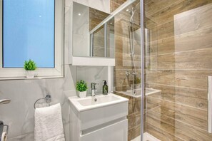 Ein modernes Badezimmer mit einer Duschkabine aus Glas, einem weißen Waschtisch und einem Spiegel über dem Waschbecken.