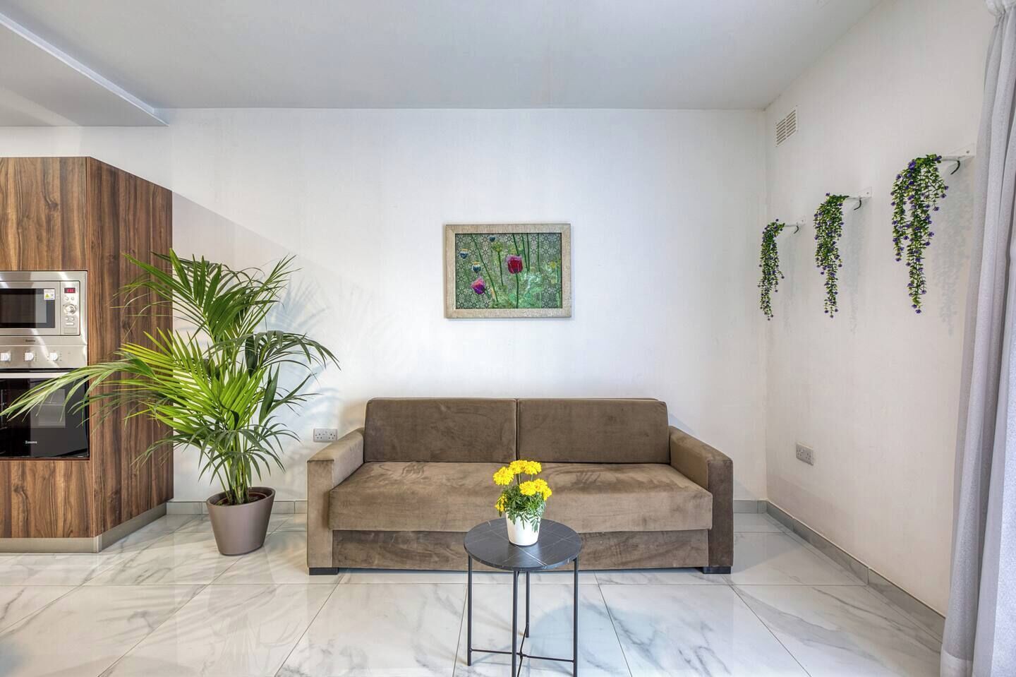 A modern living room with a sofa, a dining area with a microwave, a potted plant, and a painting on the wall.