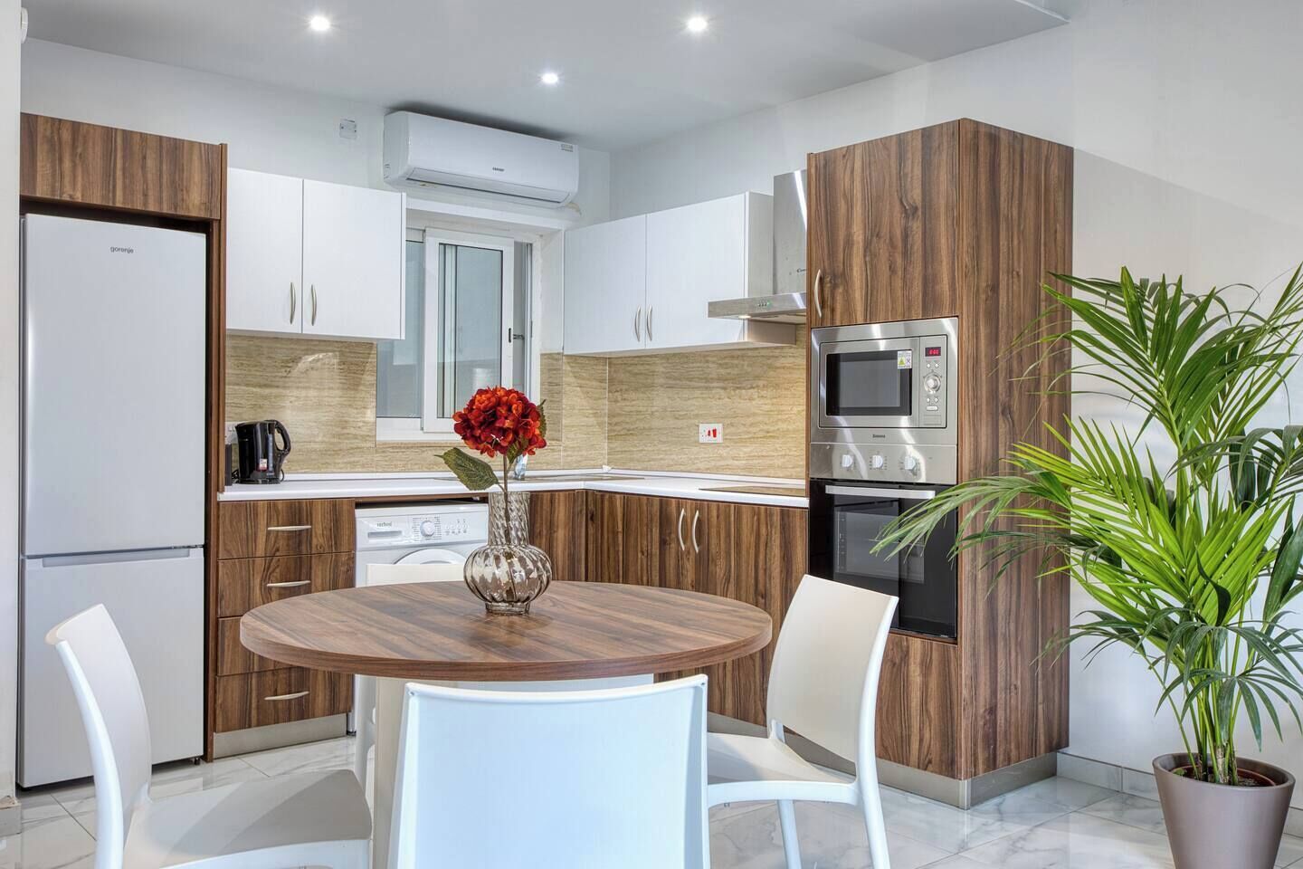 A modern kitchen with wooden cabinets, a built-in oven, and a dining area with a round table and chairs.
