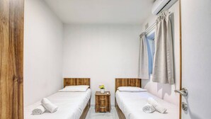 Une chambre d’hôtel avec deux lits, une petite table de chevet en bois, une fenêtre avec des rideaux et une porte.