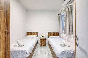 Ein Hotelzimmer mit zwei Betten, einem kleinen Nachttisch aus Holz, einem Fenster mit Vorhängen und einer Tür.