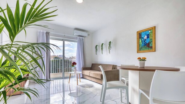 Una sala moderna con sofá, una mesa de comedor, sillas, un balcón con vistas y un cuadro en la pared.