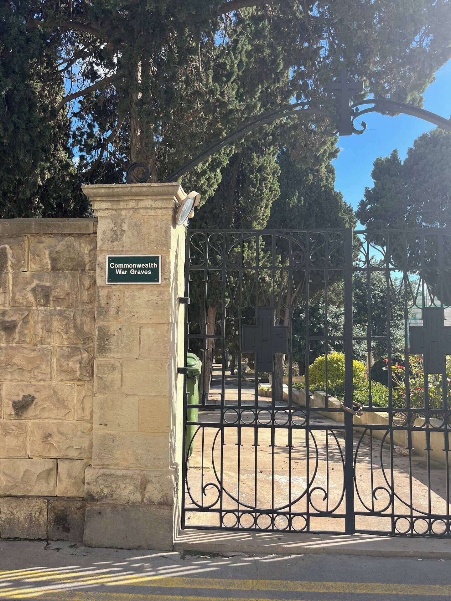 A wrought iron gate with a stone wall and a sign that reads 'Commonwealth War Graves.'