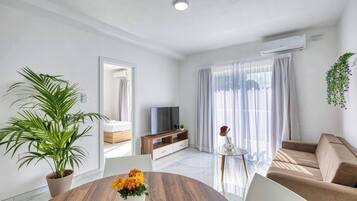 A modern living room with a TV, sofa, and a dining table with flowers.