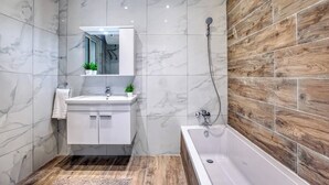 Un baño moderno con tocador de mármol, pared decorativa de madera y bañera independiente.