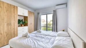 Un dormitorio con cama, armario, planta en maceta y ventana con cortinas.