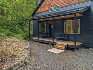 En stuga med en inglasad veranda, ett trädäck och en mur av sten som fungerar som stödmur.