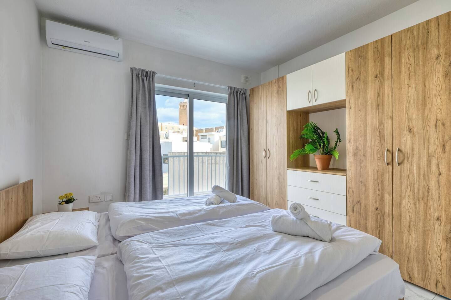 A hotel room with a bed, a wardrobe, a potted plant, and a window with curtains.