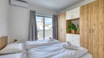 A hotel room with a bed, a wardrobe, a potted plant, and a window with curtains.