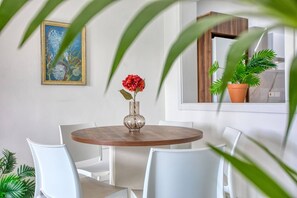 A dining area with a round wooden table, white chairs, a vase with a red flower, and a painting on the wall. - Modern, Central 3-BR Apt with Valletta View (Tal-Pietà)