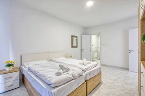 A bedroom with a double bed, a bedside table with a lamp, a mirror on the wall, and a door leading to a bathroom. - Modern, Central 3-BR Apt with Valletta View (Tal-Pietà)