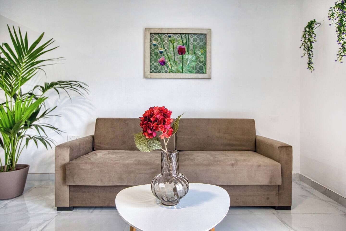 A modern living room with a sofa, a glass vase with flowers, and a potted plant.