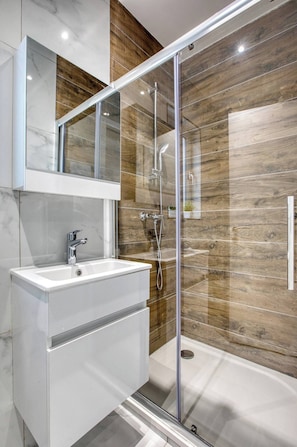 A modern bathroom with a glass-enclosed shower, a white vanity, and a wooden wall panel. - Modern, Central 2-BR Apt with Valletta View (Tal-Pietà)