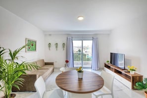 A modern living room with a sofa, a dining table with chairs, a TV, and a balcony with curtains. - Modern, Central 2-BR Apt with Valletta View (Tal-Pietà)