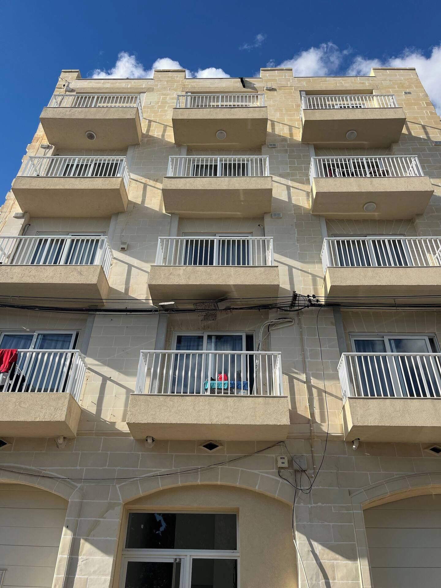 A multi-story building with balconies, a central entrance, and a clear sky.