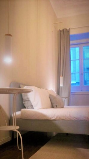 Ein Zimmer mit einem Bett, einem Nachttisch und einem fensterbepflanzten Fenster.