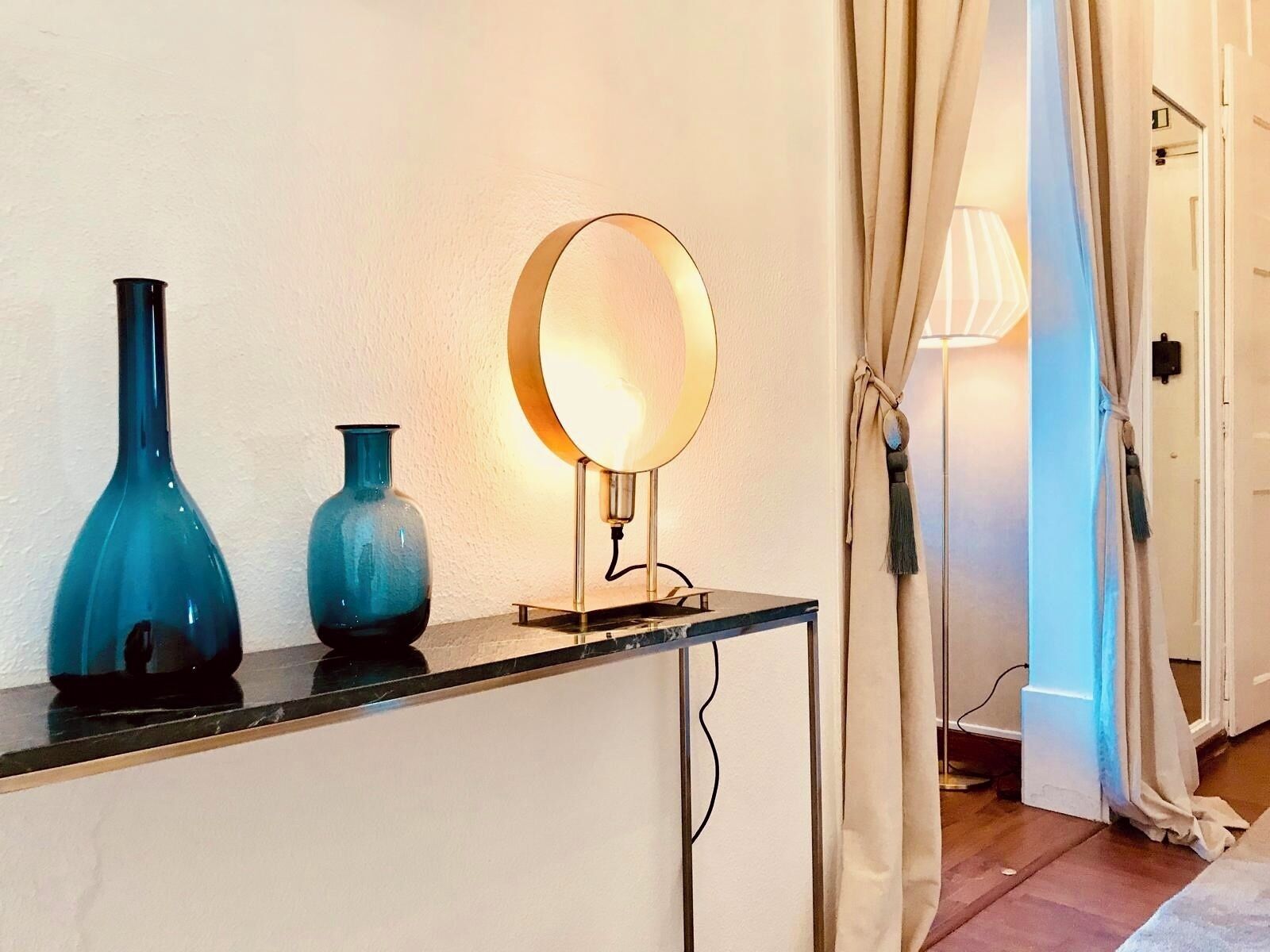 A room with a mirror on a stand, two blue vases on a counter, and a door with curtains.